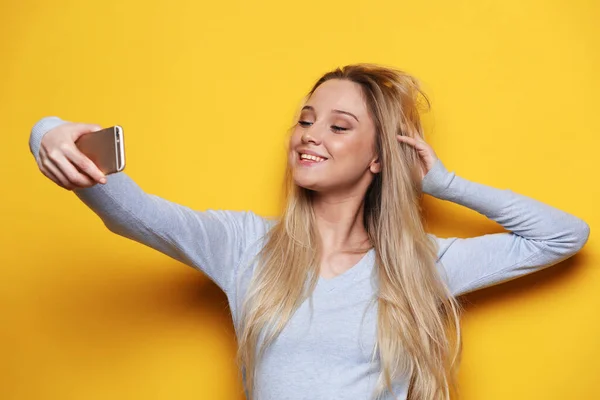 Ung leende blond kvinna gör selfie på gul bakgrund. — Stockfoto