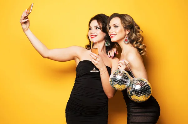 2人の笑顔の女の子がパーティーを開きスマートフォンで自撮りし黄色の背景で — ストック写真