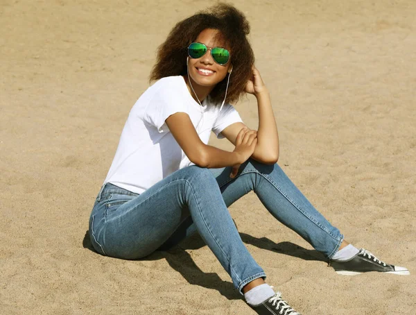 Afro amerikaanse jonge vrouw in zonnebril luisteren naar muziek in koptelefoon op haar mobiele telefoon. — Stockfoto