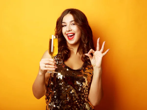 Žena ve večerních šatech drží sklo šampaňského přes žluté pozadí — Stock fotografie