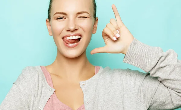 Chica divertida mostrando su lengua mientras posando sobre fondo de estudio. Emocional positiva joven hembra haciendo caras —  Fotos de Stock