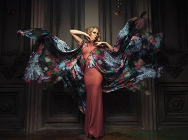 Çiçek renginde bir elbise giymiş güzel sarışın bir kadın. Çelenk desenli.