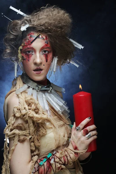 Young blond woman with creative make up holding red candle. Halloween theme. — Stock Photo, Image