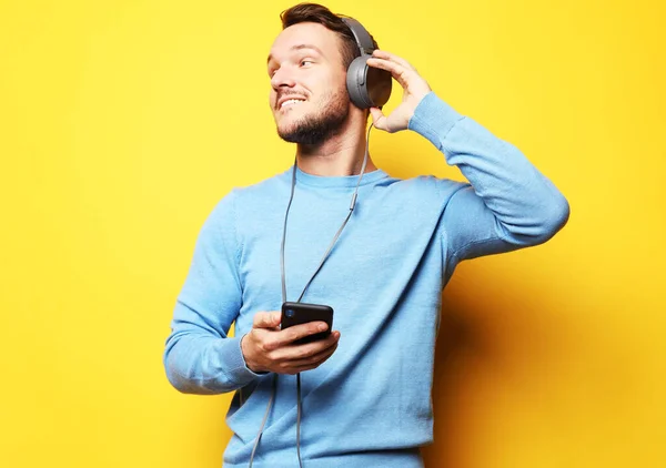 Knappe jongeman, in een blauwe trui, luisterend naar muziek over een gele achtergrond — Stockfoto
