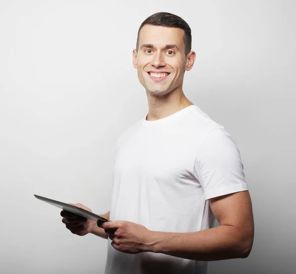 Tehnologia e conceito de estilo de vida: jovem vestindo camiseta branca usando um computador tablet isolado sobre um fundo branco — Fotografia de Stock