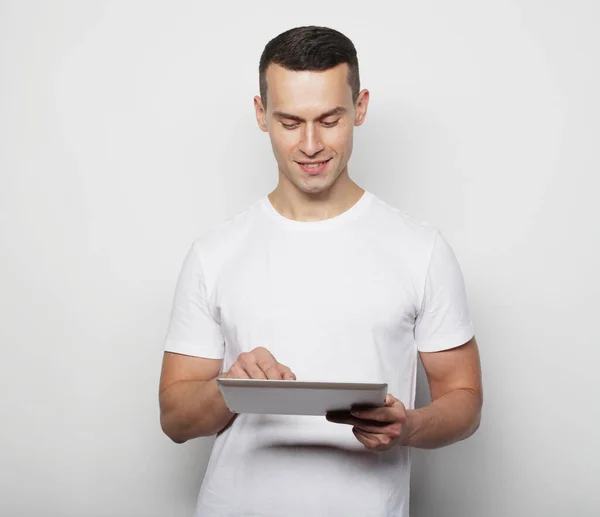 Tehnologi och livsstil koncept: ung man bär vit t-shirt med hjälp av en tablett dator - isolerad över en vit bakgrund — Stockfoto