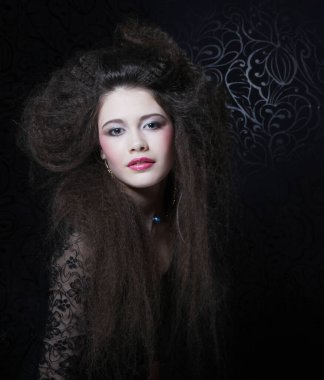 Uzun kıvırcık saçlı, akşam makyajlı, siyah elbiseli ve mücevher takan güzel bir kadın.