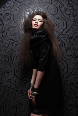 Uzun kıvırcık saçlı, akşam makyajlı, siyah elbiseli ve mücevher takan güzel bir kadın.