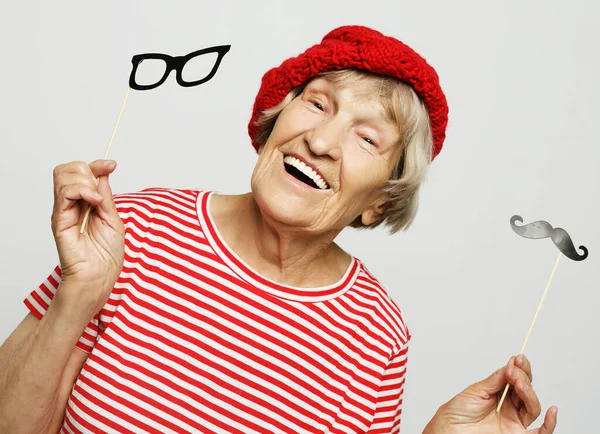 Koncepcja stylu życia i ludzi: zabawna babcia ze sztucznymi wąsami i okularami, śmieje się i przygotowuje do zabawy — Zdjęcie stockowe