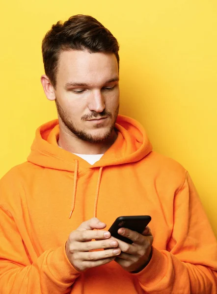 Молодой красивый мужчина держит мобильный телефон и фотографирует себя, стоя на жёлтом фоне — стоковое фото