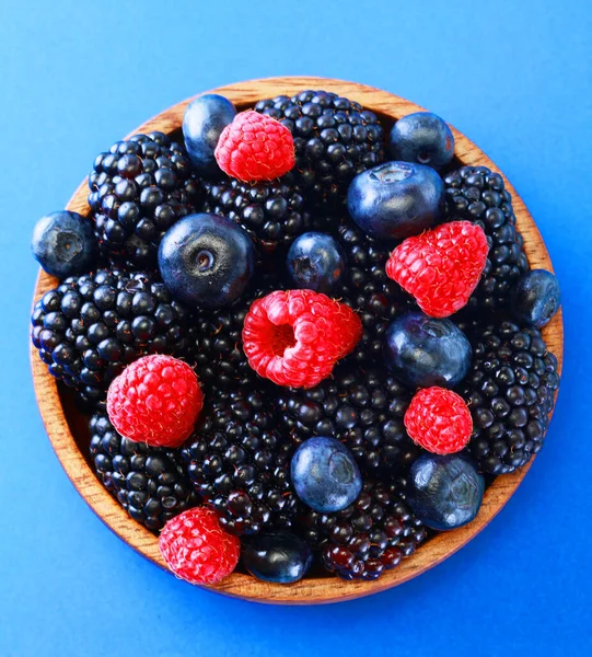 Schüssel mit frischem Obst vorhanden. Brombeeren, Himbeeren, Blaubeeren auf einer Schüssel vor blauem Hintergrund. Gesundes Frühstück. Vegane Süßspeisen. — Stockfoto