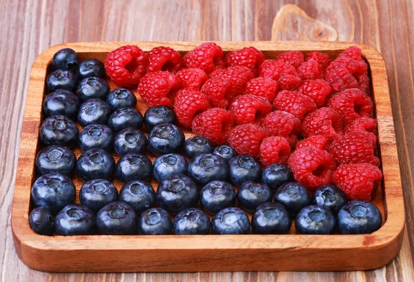 Blueberries and raspberries on wooden plate — Stock Photo, Image