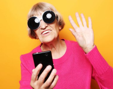 Yaşlı büyükanne torunlarıyla telefonda konuşuyor, gülümsüyor ve onları selamlıyor. Kapat..