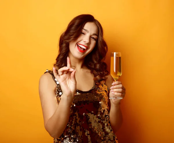 Sarı arka planda şampanya bardağı tutan gece elbiseli kadın. — Stok fotoğraf