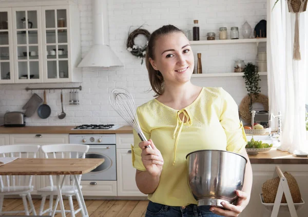 Woman in the kitchen holding a whisk and a bowl — Stock Photo, Image
