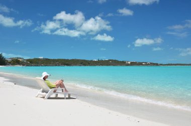Genç kadın güneş-şapkalı relax şezlong üzerinde kumlu plaj Great Exuma, Bahamas içinde