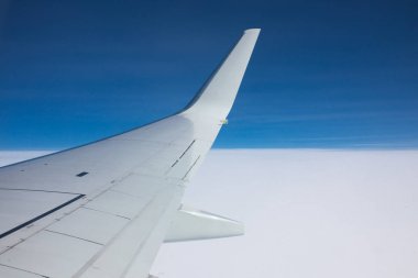 Bir uçak kanadı mavi gökyüzüne karşı pencereden görüntüleme.