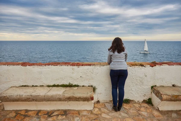 Женщина смотрит на бесконечное море и парусник — стоковое фото
