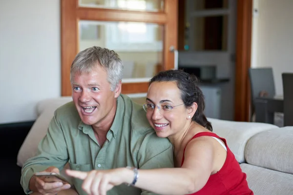 Pareja de mediana edad tienen un aspecto de un televisor en casa y feliz de ganar — Foto de Stock