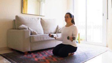 Güzel İspanyol kadın oturma odasında dambıllarıyla antrenman yapıyor.