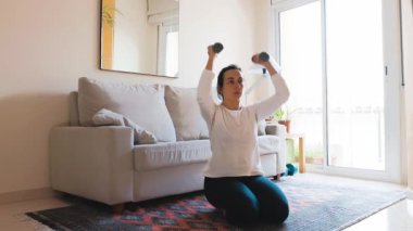 Güzel İspanyol kadın oturma odasında dambıllarıyla antrenman yapıyor.