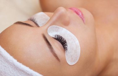 Güzellik salonunda uzun kirpikleri olan güzel bir kadın. Kirpik uzatma prosedürü. Kırbaçlar yakın.