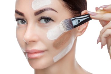 Güzel genç kadın beyaz bir arka plan üzerinde bir fırçayla yüzünde bir temel uygulama.