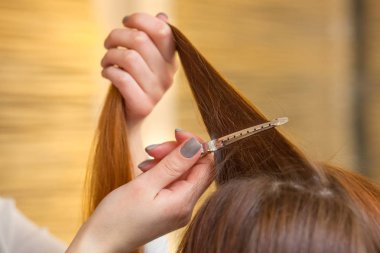 Kuaför, kuaförde müşterisinin uzun, kızıl saçlarını tarıyor. Profesyonel saç bakımı ve saç modelleri.