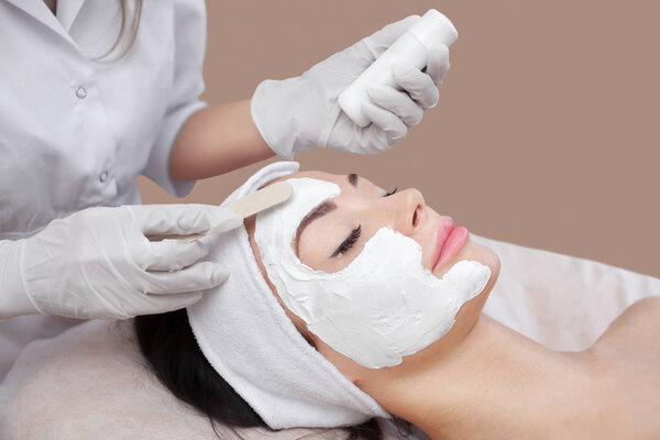 The cosmetologist for procedure of cleansing and moisturizing the skin, applying a Alginic mask to the face of a young woman in beauty salon.Cosmetology and professional skin care.