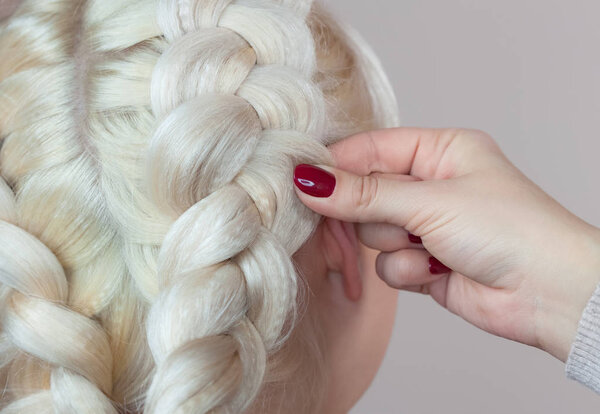 Beautiful girl with blonde hair, hairdresser weaves a  braid close-up, in a beauty salon. Professional hair care and creating hairstyles.