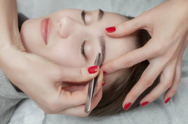 Makyöz, güzellik salonundaki genç bir kadının kaşlarını alıyor. Profesyonel cilt bakımı ve makyaj.