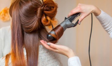 Kuaför, kuaförde uzun kızıl saçlı kuaför kız yapar. Saç maşasıyla bukleler oluşturun. Profesyonel saç bakımı..