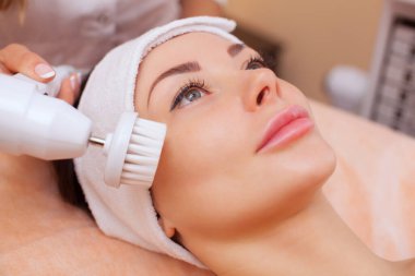 Doktor-kozmetik uzmanı bu aleti güzellik salonundaki genç ve güzel bir kadının yumuşak fırçasıyla donanım yüz temizleme prosedürü haline getiriyor. Kozmetoloji ve profesyonel cilt bakımı.