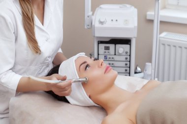 Kozmetik uzmanı, güzellik salonundaki güzel, genç bir kadının yüz derisinin mikro cilt bakımını yapıyor. Kozmetoloji ve profesyonel cilt bakımı..