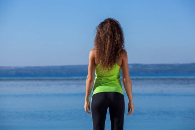 Plajda yürüyüş yaptıktan sonra siyah ve açık yeşil spor takım elbiseli genç ve zayıf kız oturuyor. Sağlıklı yaşam tarzı ve vücut bakımı kavramı.