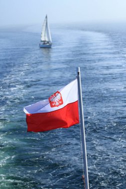 Arka planda bir yat ile denizde bir gemi direği üzerinde sallayarak Polonya bayrağı