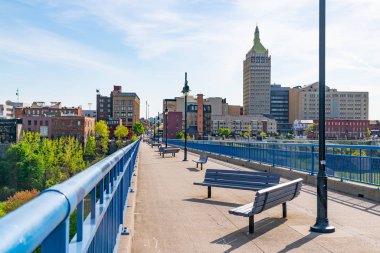 ROCHESTER, NY - MAY 14, 2018: Skyline of Rochester, New York along the Pont De Rennes Pedestrian Bridge which is part of the Genesee Riverway Trail clipart