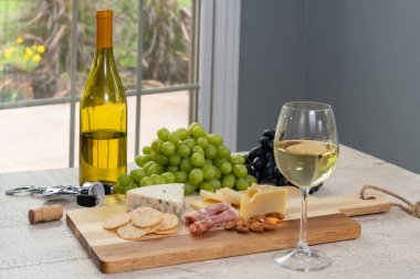 Bardak beyaz şarap şişe şarap, peynir, kraker, jambon, badem ve üzüm ile