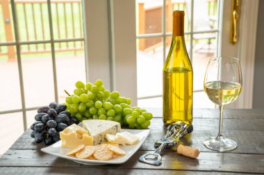 Bardak beyaz şarap şişe şarap, peynir ve üzüm ile
