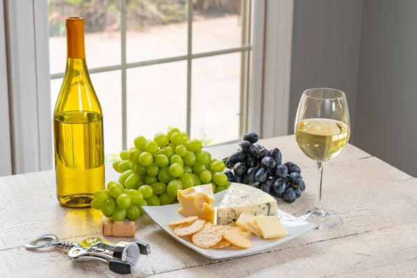 Bardak beyaz şarap şişe şarap, peynir ve üzüm ile