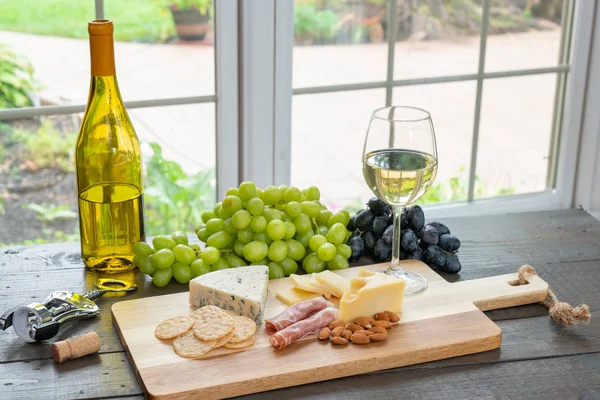 Glass of white wine with wine bottle, cheese, crackers, almonds and grapes