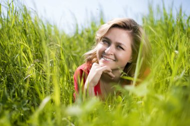 kırmızı elbiseli bir kız yaz aylarında bir alanda yeşil çim oturur ve kameraya bakar