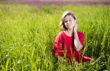 yaz aylarında bir alanda yeşil çim oturan kırmızı elbiseli bir kız