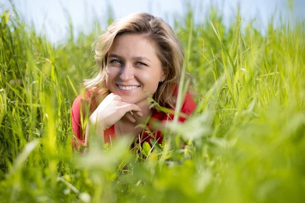 A girl in a red dress sits in the green grass in a field in the summer and looks at the camera Royalty Free Stock Images