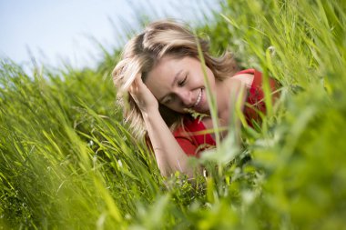 yaz aylarında bir alanda yeşil çim oturan kırmızı elbiseli bir kız
