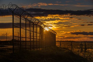 gün batımında alanda dikenli tel ile kapalı metal çit