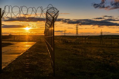 gün batımında alanda dikenli tel ile kapalı metal çit