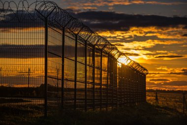 gün batımında alanda dikenli tel ile kapalı metal çit