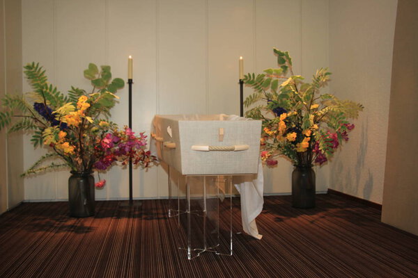 A modern casket in a funeral home with flowers and candles
