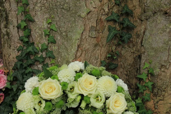 white sympathy wreath or funeral flowers near a tree, white roses and mums